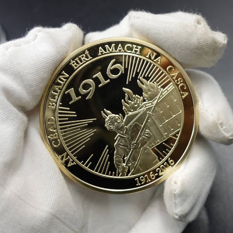 Dark and gold-tone historical anniversary coin with 1916 and 1916-2016 dates, a standing figure and Irish-language rim lettering