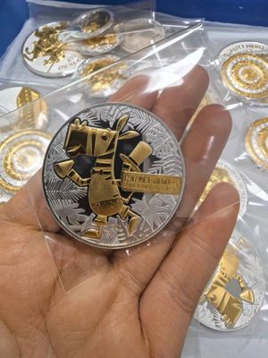 Silver-tone round coin with gold-tone raised giraffe mascot and tropical leaf detail, held in protective film
