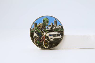 Full-color illustrated coin showing a green-faced rider on a motorcycle against a city street and car