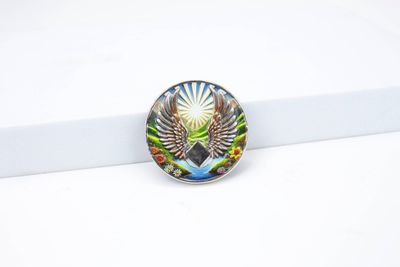 Round coin showing wide multicolored eagle wings, bright radiating sunbeams and colorful landscape accents