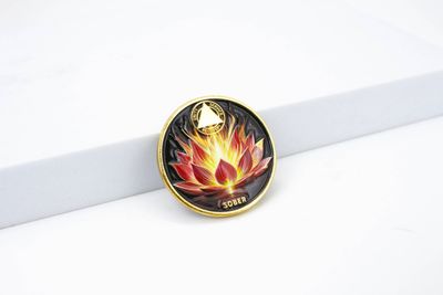 Black coin face with a gold rim and colorful orange-red lotus/flame motif over the small word SOBER