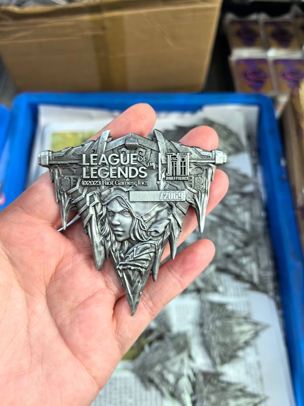 Hand holding an antique silver-look pointed fantasy gaming crest with raised lettering and sculpted faces