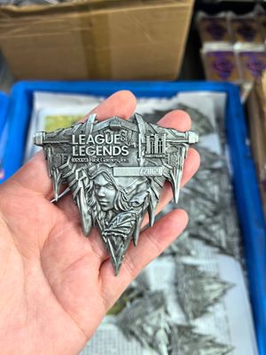 Hand holding an antique silver-look pointed fantasy gaming crest with raised lettering and sculpted faces