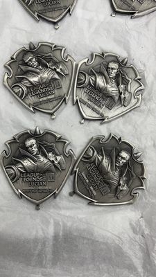 Four antique silver-look shield emblems showing raised fantasy characters and ornate pointed outlines on white fabric