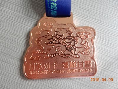 Copper-colored irregular shaped medal with Chinese dragon relief lettering and blue ribbon