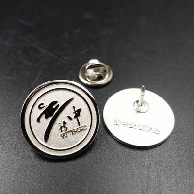 Silver circular lapel pin with black Chinese calligraphy on the front and metal pin post shown beside it