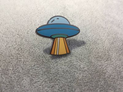 Blue cartoon flying saucer UFO shaped metal lapel pin with orange and yellow beam underneath