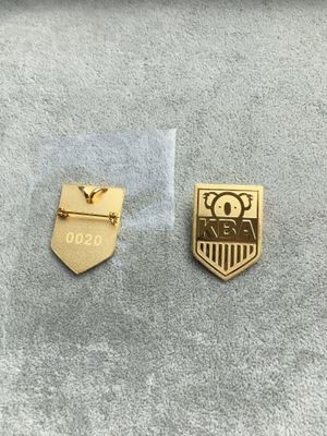 Front and reverse of gold owl crest shield lapel pin with KBA letters and 0020 marking
