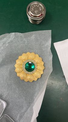 Gold flower shaped metal badge with raised petals and green circular center ornament