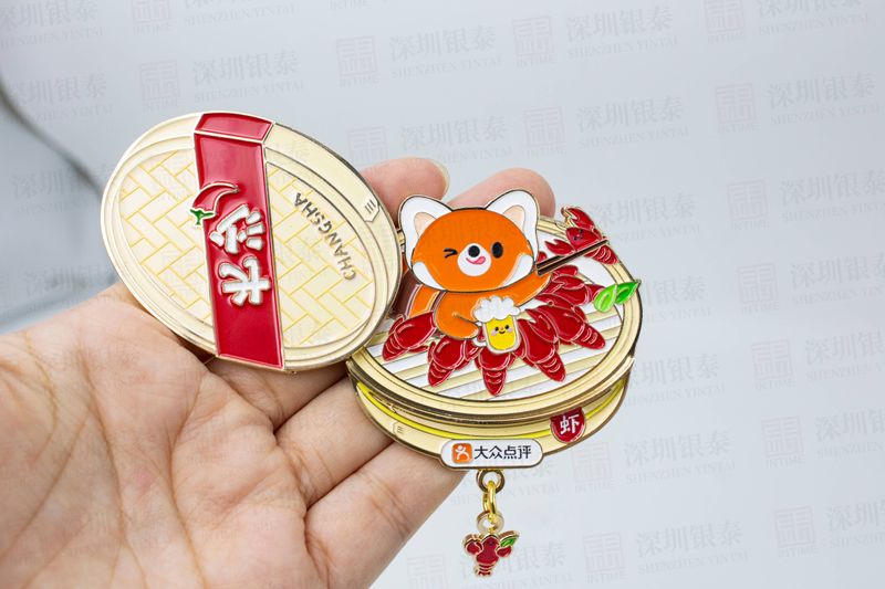 Hand holding round gold-tone mascot souvenir with red panel and dangling charm