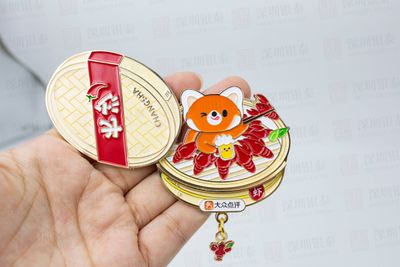 Hand holding round gold-tone mascot souvenir with red panel and dangling charm