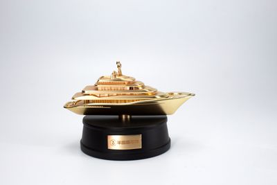 Gold-tone luxury motor yacht miniature with multi-level decks mounted on a round black presentation base