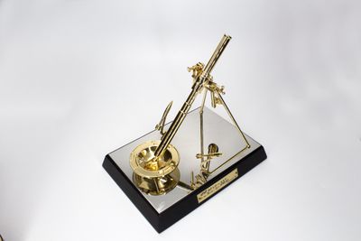 Gold-tone miniature technical instrument with long angled arm triangular supports and round detail on black display base