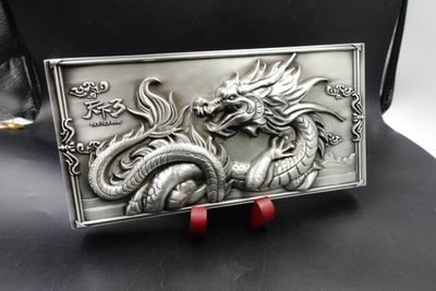 Rectangular silver-tone dragon relief plaque with ornate border standing on curved dark wood support