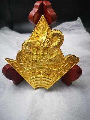 Gold-tone ornate dragon relief plaque with fan-shaped lower design mounted on a red-brown curved display support